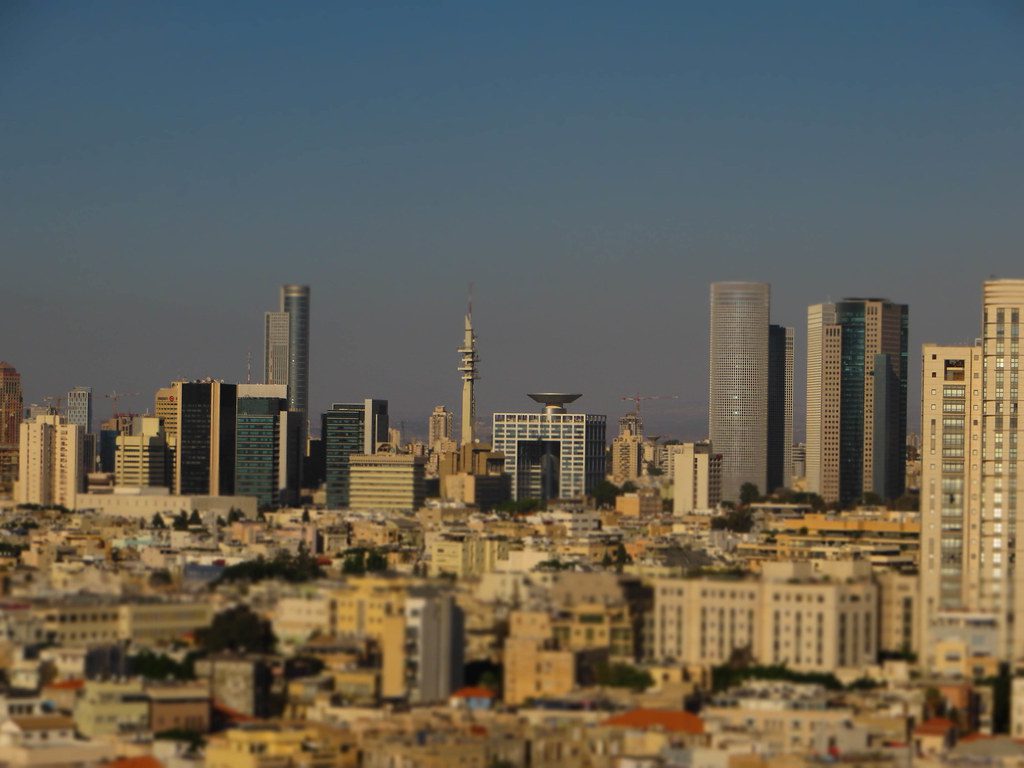 Skyline de uma cidade com arranha-céus e edifícios variados, utilizando efeito tilt-shift, que dá aspecto de miniatura.