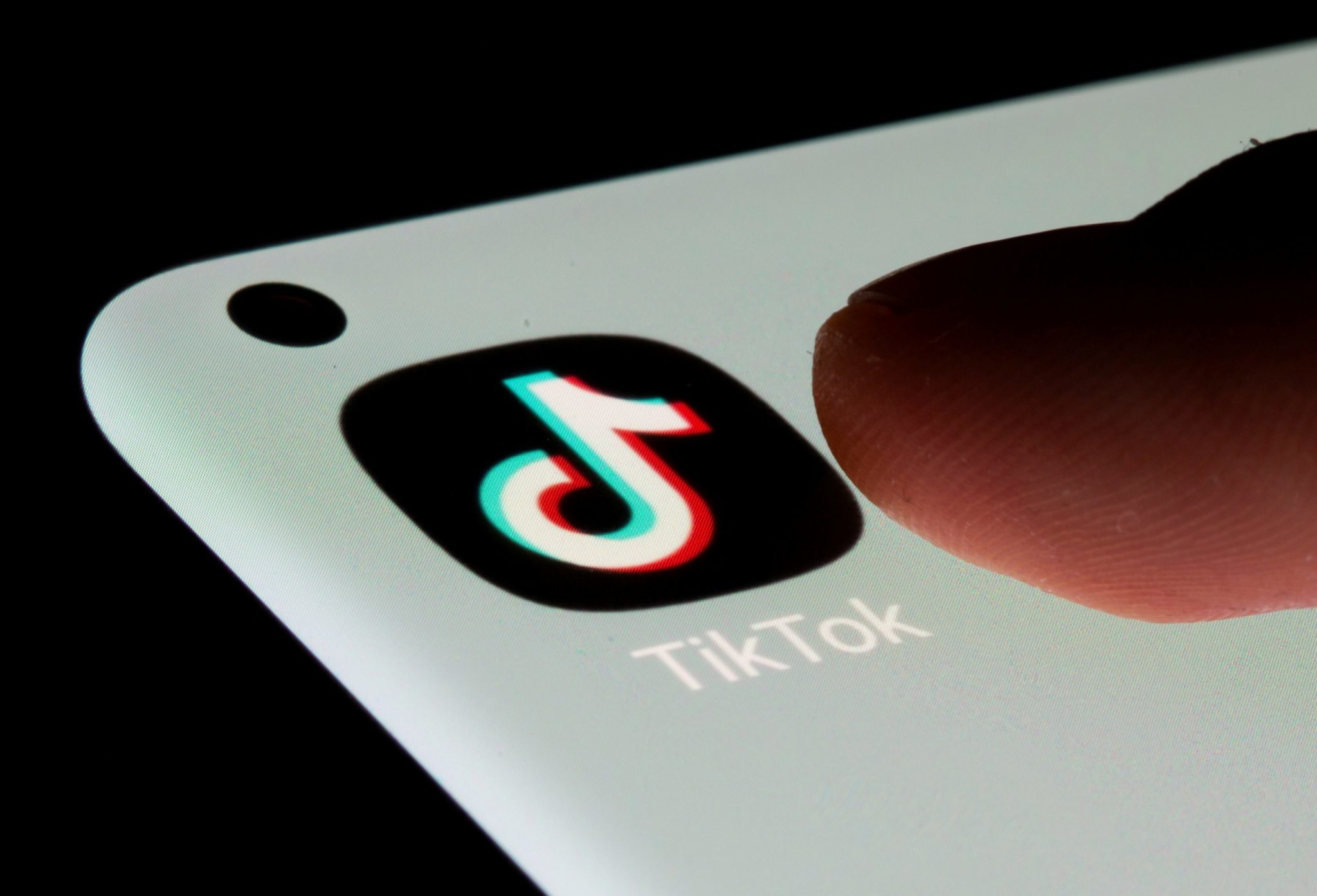 Dedo toca tela de smartphone com ícone e nome do TikTok.