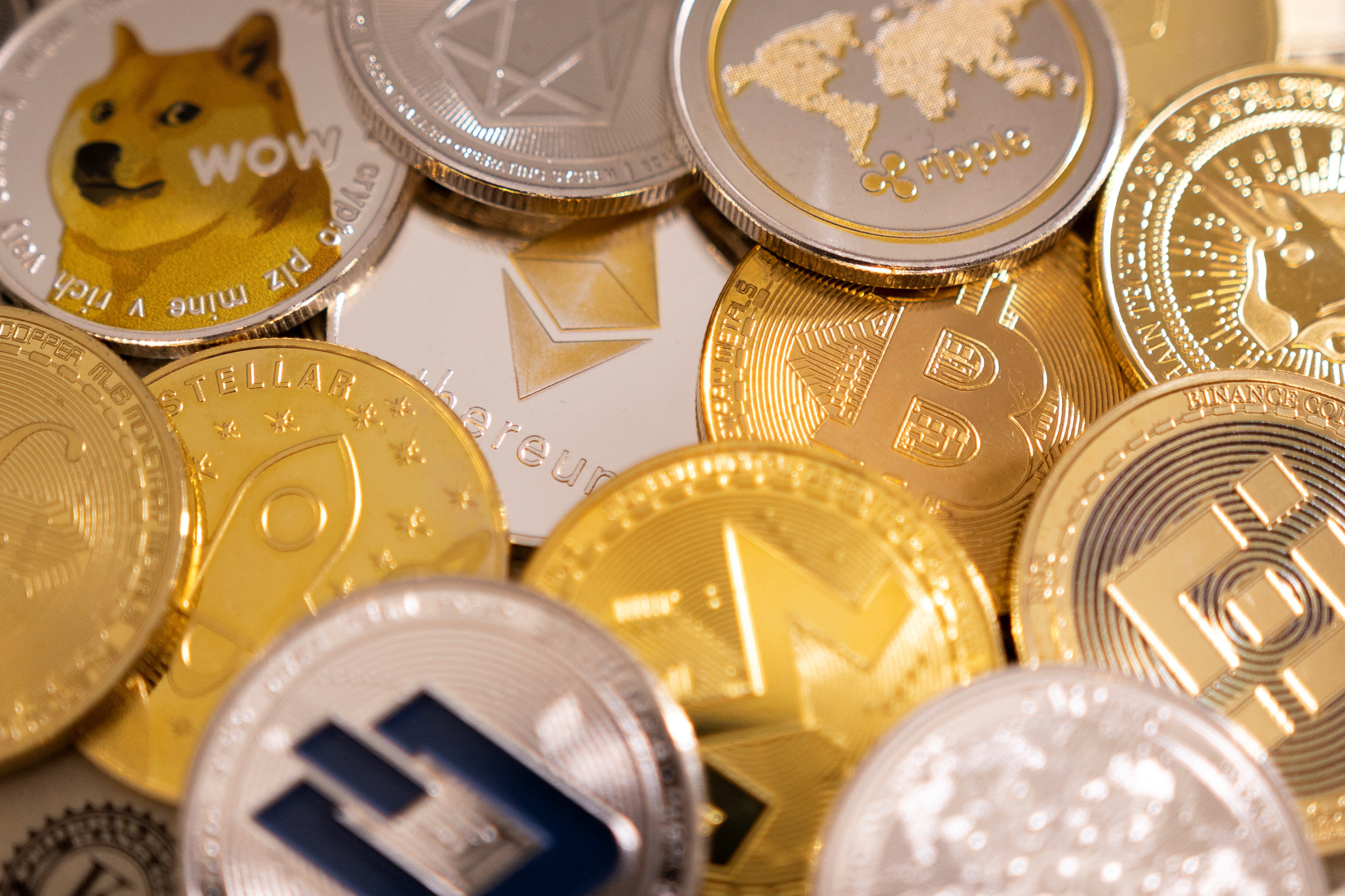 Diversas moedas físicas de criptomoeda, incluindo Dogecoin e Binance Coin, espalhadas.