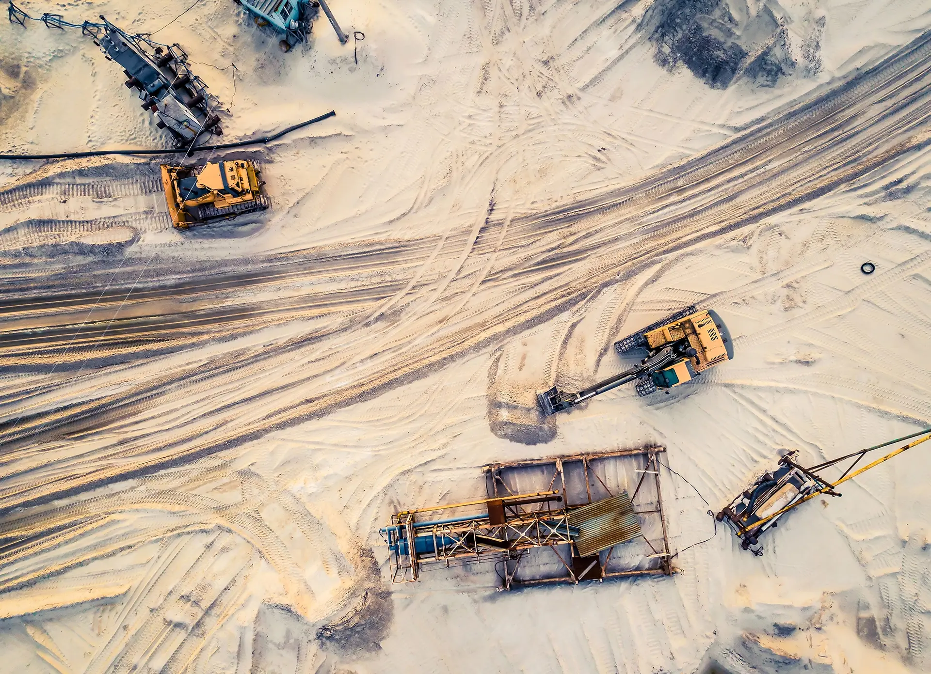 Vista aérea de maquinário pesado em operação de mineração de areia: escavadeira, trator, equipamentos diversos.