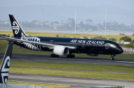 Avião preto da Air New Zealand taxiando em pátio de aeroporto, com cauda de outro avião em primeiro plano.
