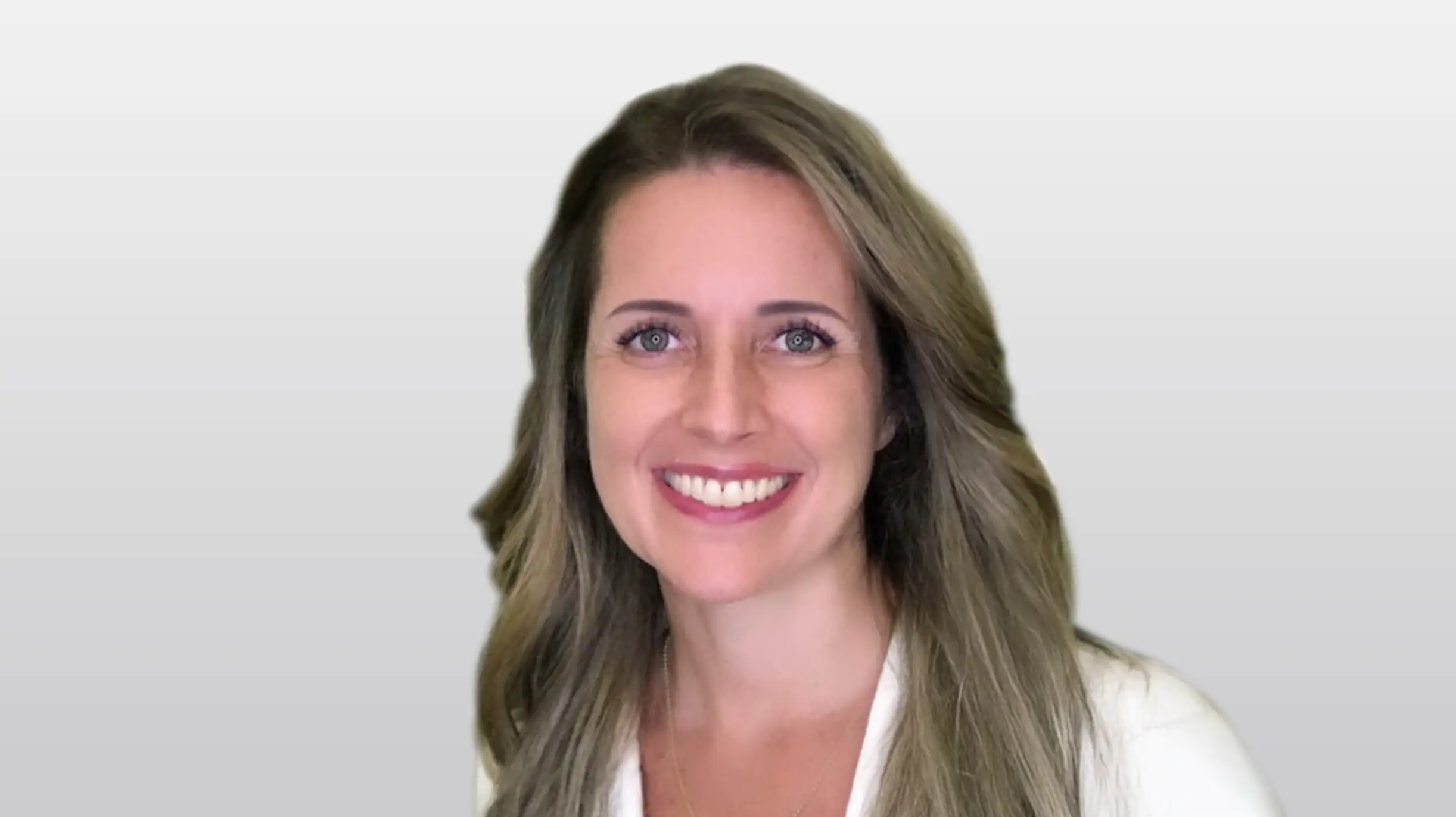 Mulher de cabelos longos e maquiagem leve sorrindo. Busto em fundo claro.