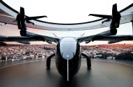 eVTOL preto em plataforma, com cidade ao entardecer no fundo.