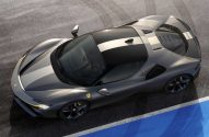 Ferrari cinza-escuro com faixas claras e detalhes amarelos, vista de cima em pista com linha azul e branca.
